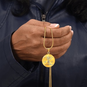 May include: A gold chain necklace with a round pendant featuring a black and white geometric design. The pendant is a sigil, a symbol used in magic and ritual.