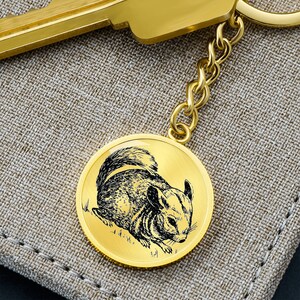 May include: Gold-toned keychain featuring a detailed engraved image of a chinchilla on a round disc.