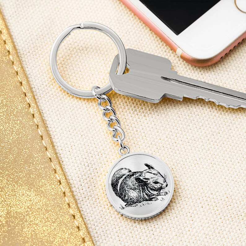 May include: A silver keychain with a round charm featuring a black and white illustration of a chinchilla. The charm is attached to a silver chain and a silver key ring.