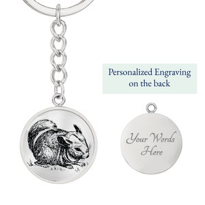 May include: Silver keychain with a round charm featuring a black and white illustration of a chinchilla. The back of the charm is blank and can be personalized with an engraving. "Personalized Engraving on the back" is written in blue text on a light green background.