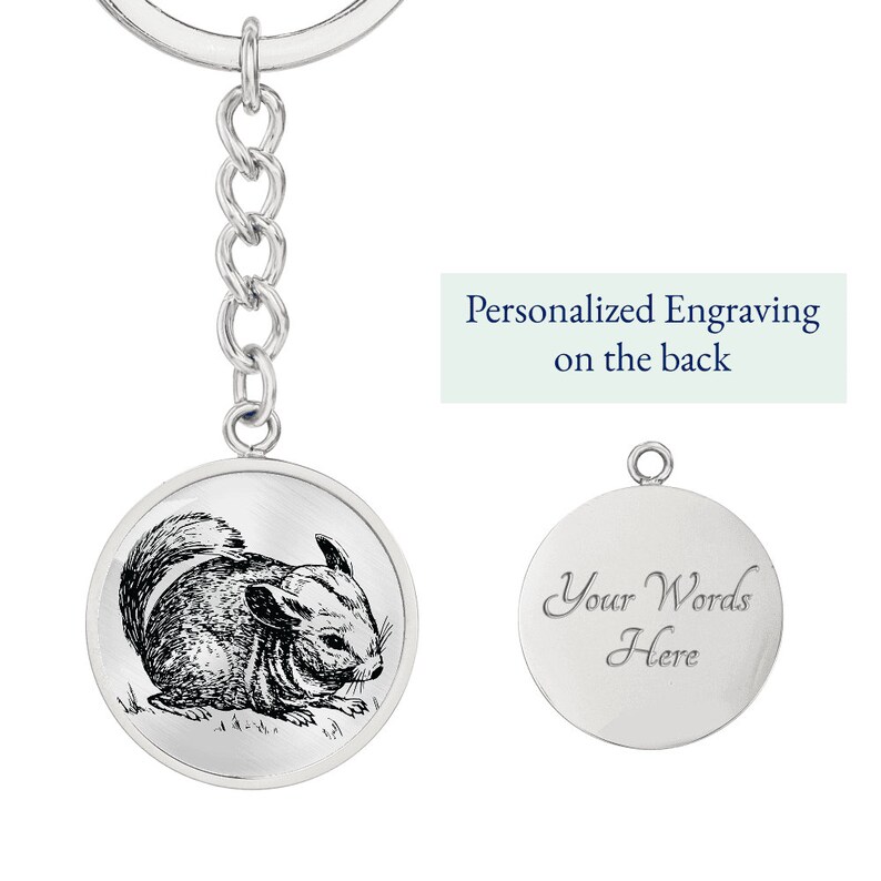 May include: Silver keychain with a round charm featuring a black and white illustration of a chinchilla. The back of the charm is blank and can be personalized with an engraving. "Personalized Engraving on the back" is written in blue text on a light green background.