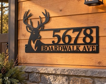 Könnte beinhalten: Ein schwarzes Metall-Adressschild mit einer Hirschkopf-Silhouette auf der linken Seite, den Ziffern 5678 in großer Schrift und dem Text BOARDWALK AVE in kleinerer Schrift darunter, alles eingefasst in einen rechteckigen Rahmen mit Befestigungsschrauben.
