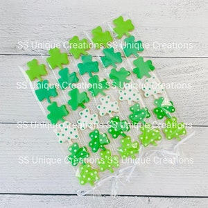 May include: Six clear cellophane bags filled with green and white shamrock-shaped cookies. The cookies are decorated with green and white polka dots. The bags are tied with white ribbon. The text "SS Unique Creations" is printed on the bags.