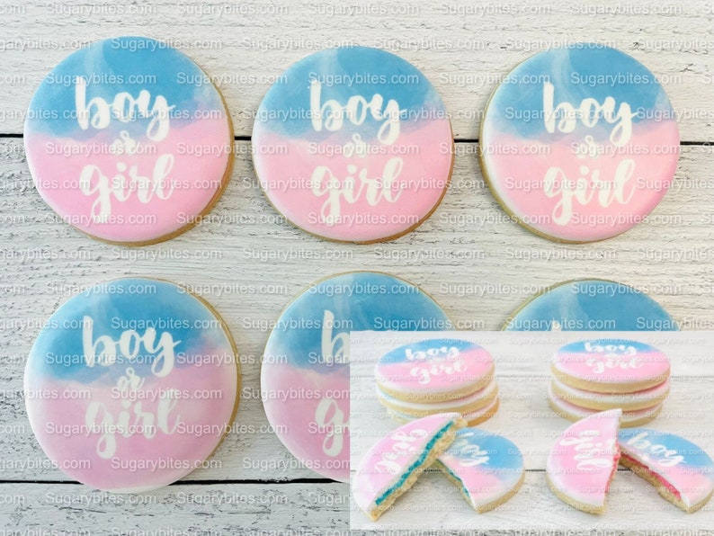 May include: Six round sugar cookies decorated with blue and pink icing. The cookies are decorated with the words "boy or girl" in white icing. Three of the cookies are stacked on top of each other. The cookies are on a white wooden surface.