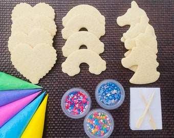 Op de afbeelding: Een set voor het versieren van koekjes, inclusief eenvoudige suikerkoekjes in de vorm van harten, regenbogen en eenhoorns, samen met kleurrijke sprinkles en spuitzakken.