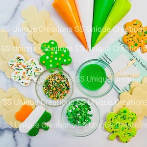 May include: A DIY cookie decorating kit with green, white, and orange icing, green sprinkles, and sugar crystals. The kit includes four sugar cookies shaped like shamrocks, a card with instructions, and a small bowl of green sprinkles.