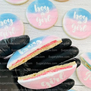 May include: Two sugar cookies decorated with blue and pink icing. The cookies are split in half to show the inside of the cookie. One cookie is decorated with the words "boy or girl" and the other cookie is decorated with the words "it's a girl".