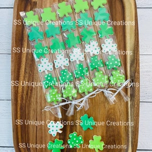 May include: A tray of individually packaged green shamrock cookies. The cookies are decorated with green and white polka dots. The packages are tied with white ribbon and labeled "SS Unique Creations".