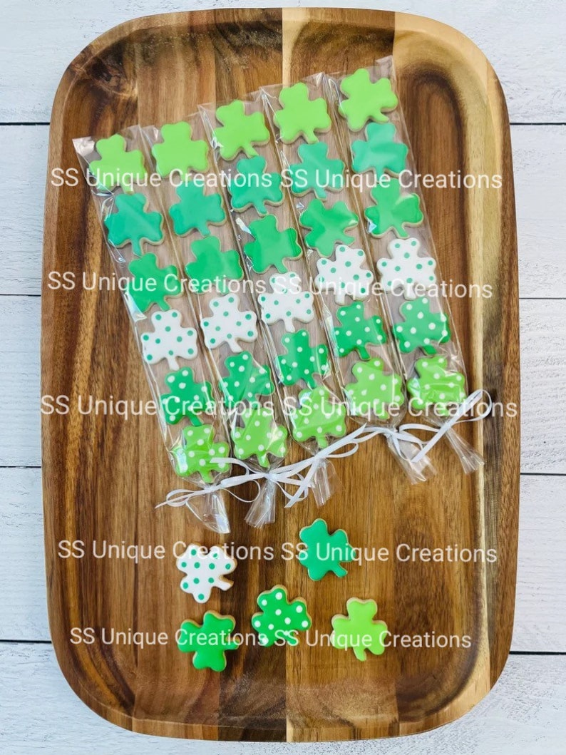 May include: A tray of individually packaged green shamrock cookies. The cookies are decorated with green and white polka dots. The packages are tied with white ribbon and labeled "SS Unique Creations".