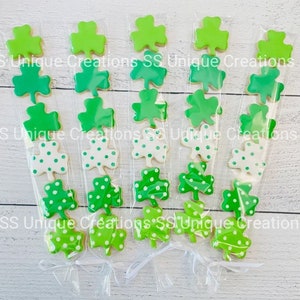 May include: Five clear cellophane bags filled with green shamrock cookies. The cookies are decorated with green and white polka dots. The bags are tied with white ribbon.