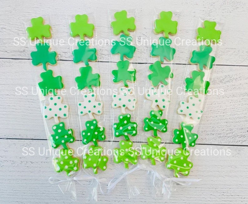 May include: Five clear cellophane bags filled with green shamrock cookies. The cookies are decorated with green and white polka dots. The bags are tied with white ribbon.