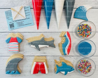 May include: A set of six decorated sugar cookies with a summer theme. The cookies are decorated with blue, red, white, and gray icing. The cookies feature a shark, a surfboard, a pair of swim trunks, and a shirt with a striped pattern. The cookies are arranged on a white wooden surface with sprinkles and piping bags.