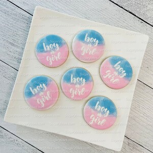 May include: A white plate with six round cookies decorated with blue and pink icing. The cookies have the text "boy or girl" written in white icing.