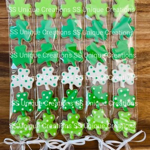 May include: Six clear cellophane bags filled with green and white shamrock-shaped cookies. Each bag is tied with a white ribbon and has the text "SS Unique Creations" printed on it.