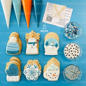 Puede incluir: Una vista aérea de galletas con temática invernal y suministros de decoración. Las galletas incluyen un muñeco de nieve, una bola de nieve, un guante y un copo de nieve. También se ven mangas pasteleras y chispas en cuencos pequeños.
