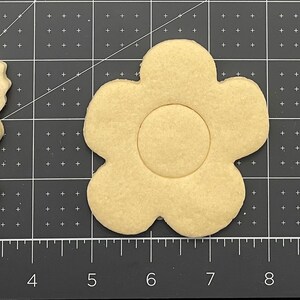 Op de afbeelding: Drie houten koekjesvormen in de vorm van een vlinder, een bloem en een tulp. De vormen zijn beige van kleur en zijn gerangschikt op een zwart-wit raster.