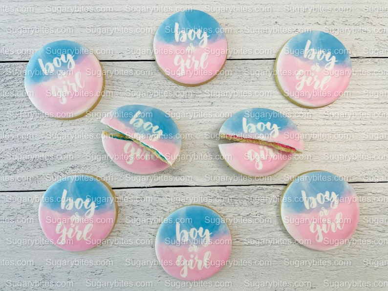 May include: Nine round sugar cookies decorated with blue and pink icing. The cookies are decorated with the words "boy or girl" in white icing.