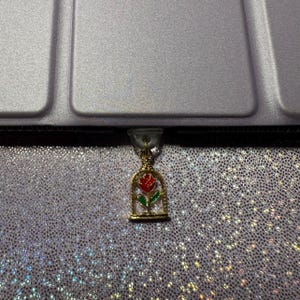 May include: A gold charm with a red rose inside a glass dome. The charm is hanging from a zipper pull.