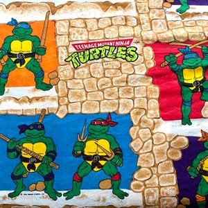 May include: A patterned fabric featuring the Teenage Mutant Ninja Turtles. The design includes the turtles in various poses, each with their signature weapons, set against a backdrop of stone walls and colourful panels. The words "Teenage Mutant Ninja Turtles" are also visible.