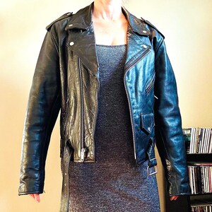 May include: A black leather motorcycle jacket with a zipper closure and multiple pockets. The jacket has a classic biker style and features a silver zipper and snaps.