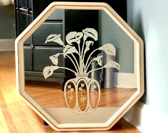 May include: Octagonal mirror with a white frame and a floral design etched into the glass. The design features a vase with flowers.