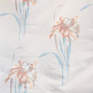 May include: A white fabric with a repeating pattern of light brown and peach colored iris flowers with light blue stems and leaves.