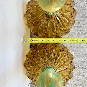 Pu&ograve; includere: Due basi per lampada in vetro color ambra con una texture profondamente scanalata e plissettata. Un metro a nastro giallo Stanley &egrave; posizionato al centro, indicando una larghezza di circa 28 cm per la coppia di oggetti in vetro insieme.