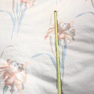May include: A white fabric with a floral pattern of light brown and beige flowers. A yellow measuring tape is placed vertically on the fabric, measuring 18 inches.
