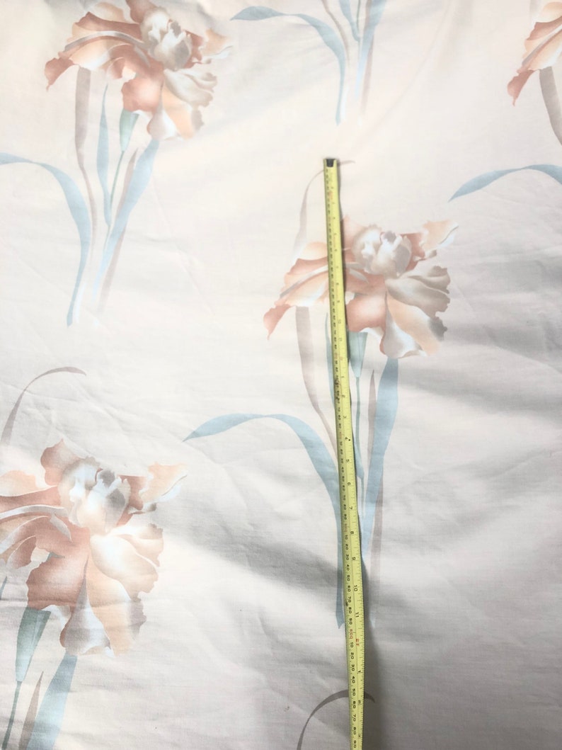 May include: A white fabric with a floral pattern of light brown and beige flowers. A yellow measuring tape is placed vertically on the fabric, measuring 18 inches.