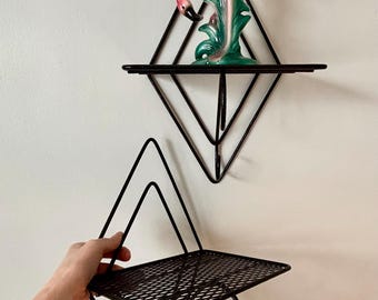 May include: Black metal diamond-shaped wall shelves. One shelf has a pink and green flamingo figurine. The shelves have a wire mesh surface. The design is geometric and retro.