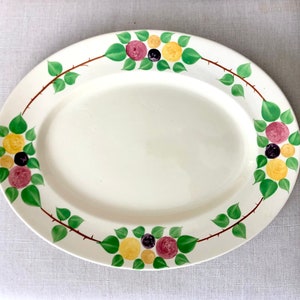 Peut inclure: Un plat de service ovale blanc avec un motif floral vert, jaune et violet autour du bord.