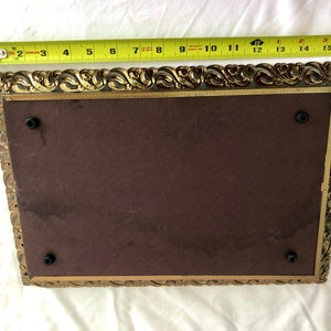 May include: An antique rectangular picture frame with an ornate gold-coloured filigree border. The frame has a dark brown backing and measures approximately 40 cm long.