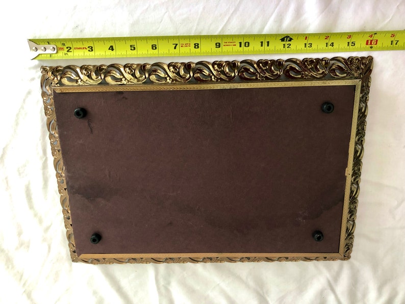 May include: An antique rectangular picture frame with an ornate gold-coloured filigree border. The frame has a dark brown backing and measures approximately 40 cm long.