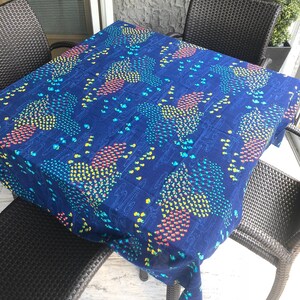 May include: A blue tablecloth with a colorful geometric pattern. The tablecloth is on a table with two black wicker chairs.