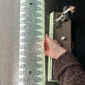 May include: A long, rectangular wall light fixture featuring a textured, clear glass shade with a repeating white geometric triangular pattern. The fixture includes a metallic base with a single light socket and a central mounting knob for installation.