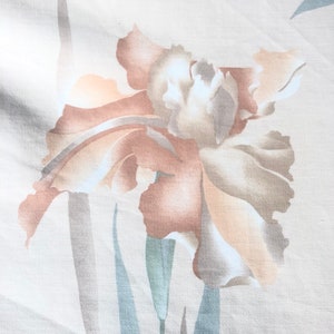 May include: A beige fabric with a light brown and white floral print. The flower is a stylized iris with a light brown stem and leaves.