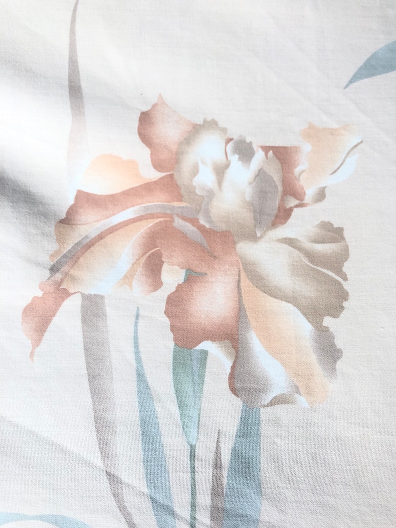 May include: A beige fabric with a light brown and white floral print. The flower is a stylized iris with a light brown stem and leaves.