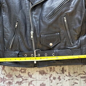 May include: Black leather motorcycle jacket with a zipper closure, two pockets, and a belt with a buckle. The jacket is measured with a yellow tape measure.