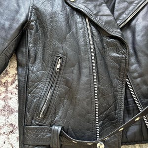 May include: Black leather motorcycle jacket with a zipper closure, a belt, and a zippered pocket on the left side.