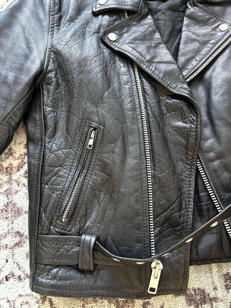 May include: Black leather motorcycle jacket with a zipper closure, a belt, and a zippered pocket on the left side.