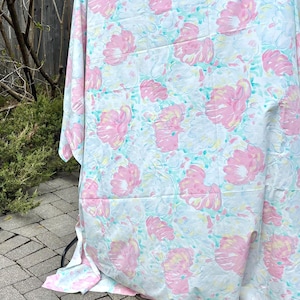 May include: A floral patterned fabric in shades of pink, white, and light blue. The design features large, stylized flowers with yellow accents on a light blue background. The fabric is draped over an unseen object.