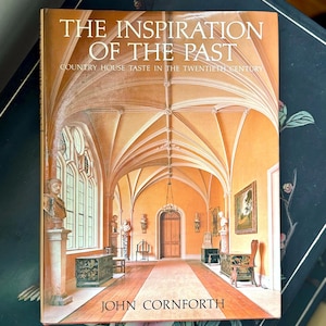 May include: A book titled "The Inspiration of the Past: Country House Taste in the Twentieth Century" by John Cornforth. The cover features a photograph of a grand, arched hallway with a wooden floor and a large, arched doorway at the end.