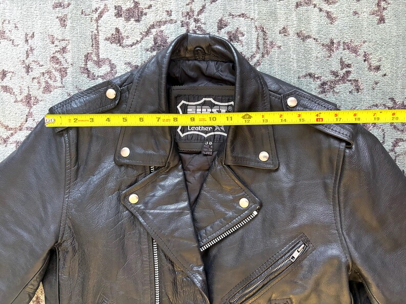 May include: Black leather motorcycle jacket with a zipper closure and multiple pockets. The jacket has a label that reads "First Leather Apparel".