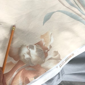 May include: Close-up of a beige fabric with a floral pattern. The fabric features large, abstract flowers in shades of brown, beige, and white. The fabric has a subtle sheen and a soft texture.