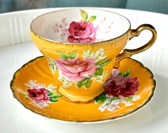 May include: A yellow teacup and saucer set with a floral pattern of pink roses and green leaves. The cup and saucer have a gold trim.