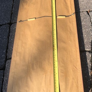 May include: The back of a framed picture with a brown mount and a red wood frame. A yellow measuring tape is placed along the right side of the frame. The tape measures 25.4 cm.