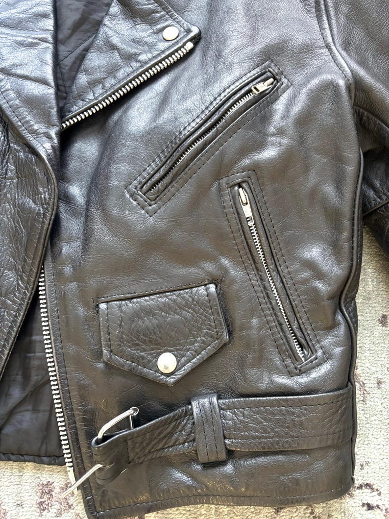May include: Black leather motorcycle jacket with a zipper closure, a belt, and multiple pockets.