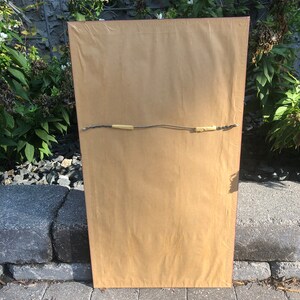 May include: The back of a framed picture with a brown paper backing and a red frame. The picture is hanging on a wall.