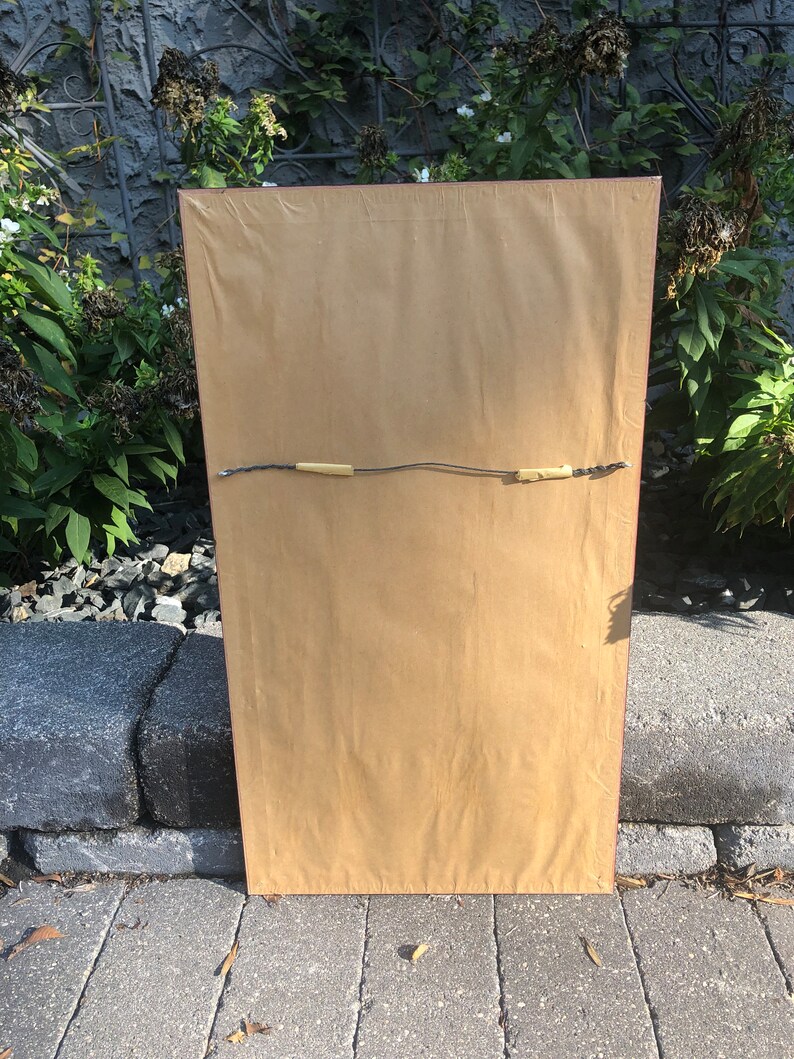 May include: The back of a framed picture with a brown paper backing and a red frame. The picture is hanging on a wall.