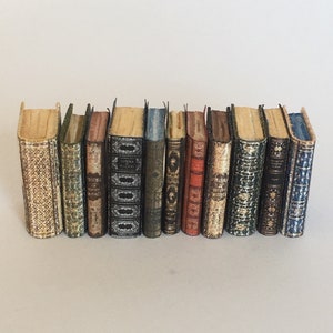 May include: A row of 12 miniature books with various colored covers and patterned designs. The books are arranged in a line on a white surface.